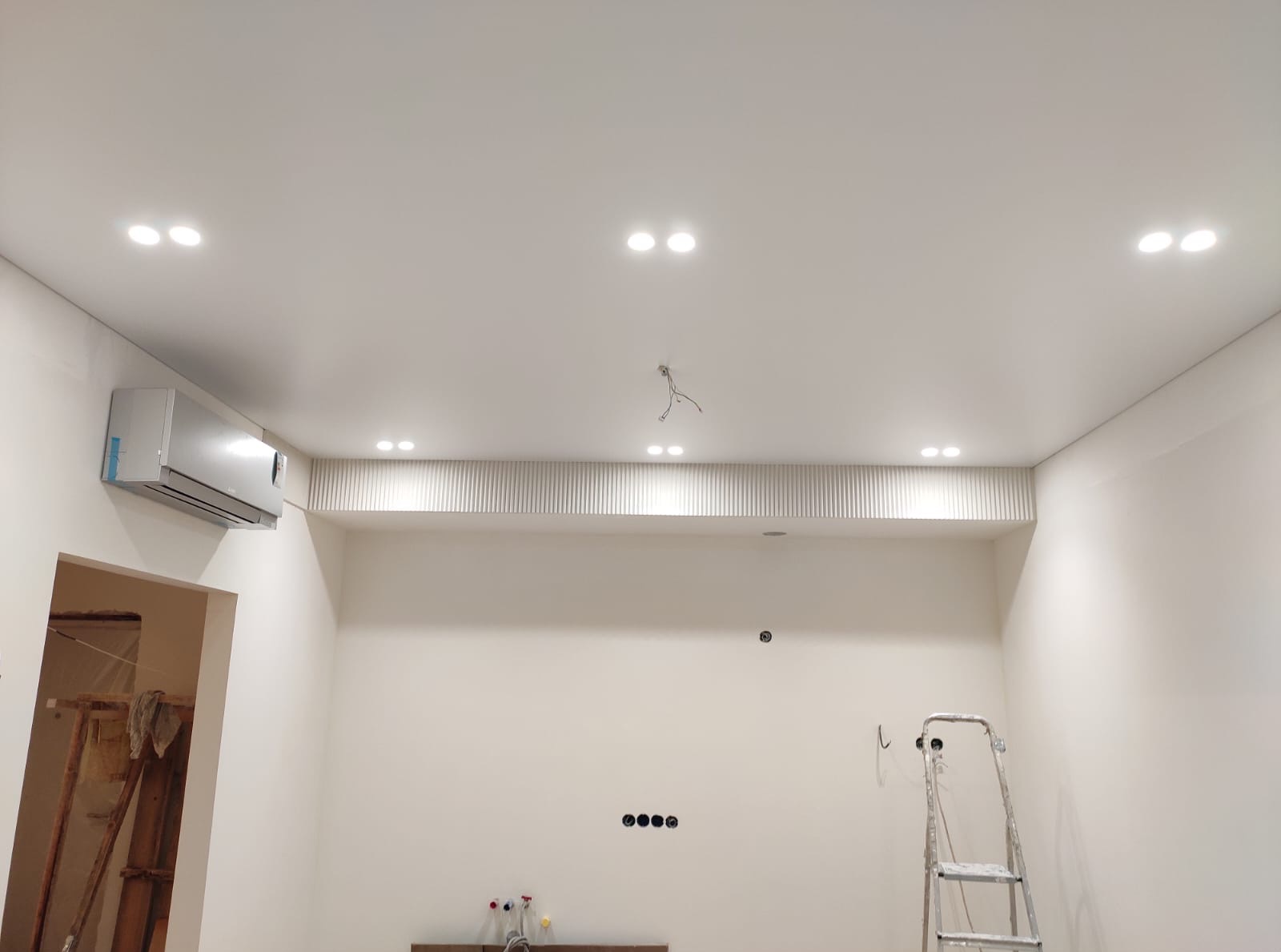 Jasne wnętrze po remoncie: białe ściany, sufit z oświetleniem punktowym i klimatyzacją. Widoczna drabina i przygotowane instalacje.