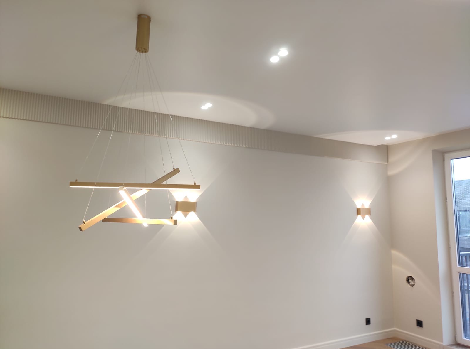 Nowoczesne oświetlenie wnętrza: designerska lampa wisząca i kinkiety ścienne w nowym mieszkaniu. Ściany w jasnym odcieniu, dekoracyjne listwy sufitowe.