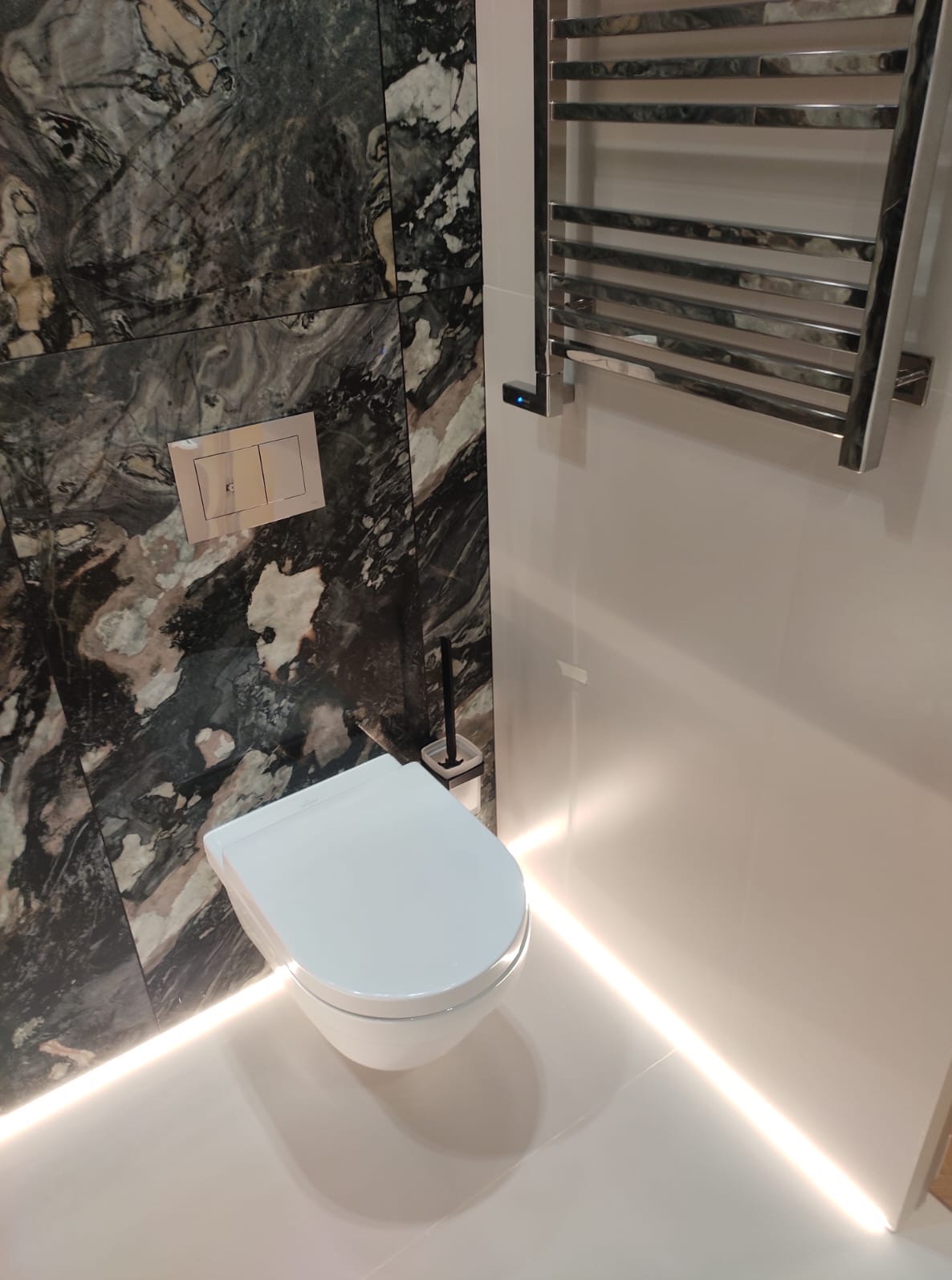 Nowoczesna łazienka: podwieszana toaleta z marmurową ścianą i podświetleniem LED, grzejnik drabinkowy. Minimalistyczny design, eleganckie wykończenie.