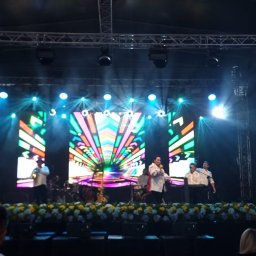 DELTA CRAFT SPÓŁKA Z OGRANICZONĄ ODPOWIEDZIALNOŚCIĄ - Zespół na scenie z kolorowym ekranem LED, nagłośnieniem i dekoracją z kwiatów oraz balonów, widok z perspektywy publiczności.