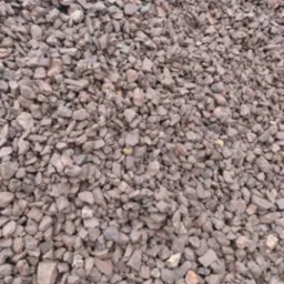 Kopalniany kruszywo o nieregularnym kształcie i brązowo-szarym kolorze, tworzące dużą pryzmę. Widoczna faktura kamieni i ich ułożenie.