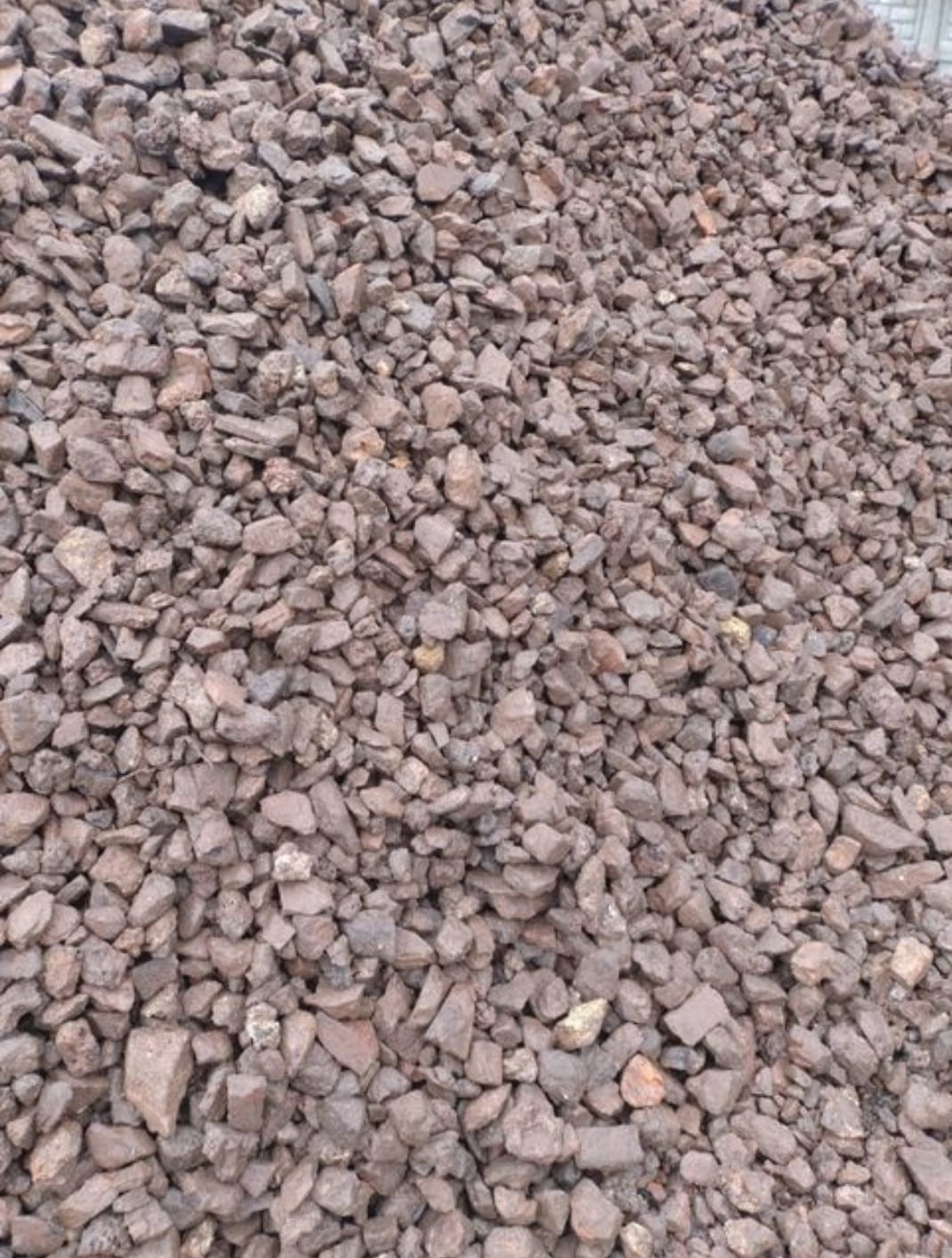 Kopalniany kruszywo o nieregularnym kształcie i brązowo-szarym kolorze, tworzące dużą pryzmę. Widoczna faktura kamieni i ich ułożenie.