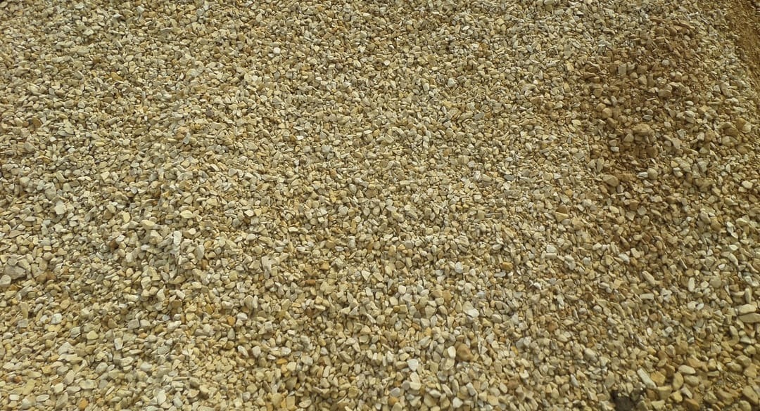 Jasny żwir o nieregularnych kształtach, drobna frakcja, równomiernie rozłożony, widok z góry, naturalne światło, delikatne cienie.