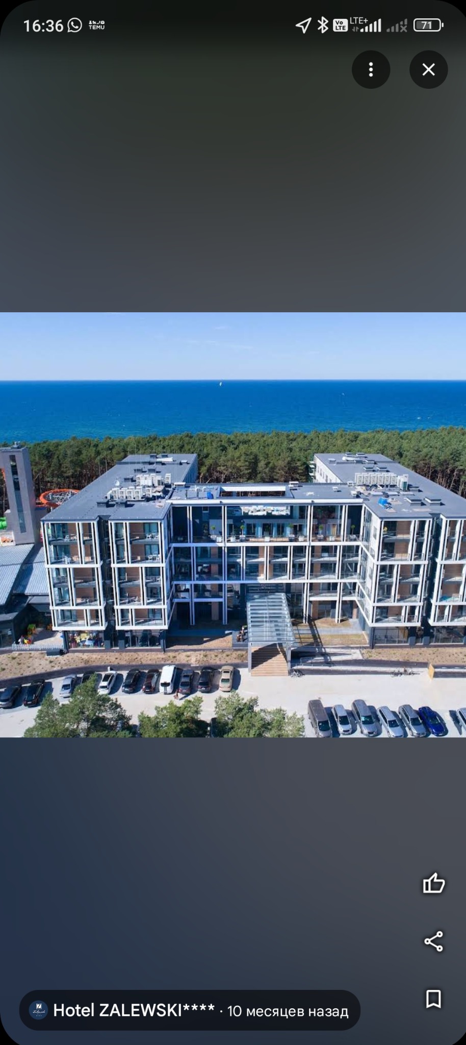 Nowoczesny, wielopiętrowy budynek hotelowy z balkonami i szklanym wejściem, na tle lasu i błękitnego morza. Widok z lotu ptaka, słoneczny dzień.