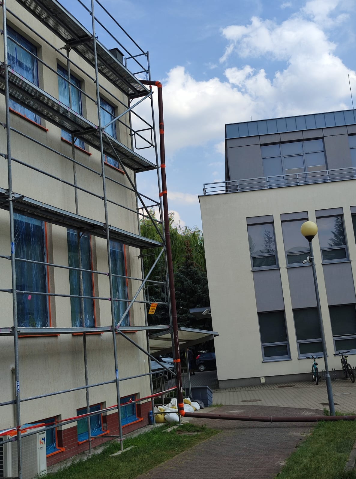 Elewacja budynku w rusztowaniach, okna zabezpieczone folią, przygotowania do prac elewacyjnych w Poznaniu, widok z dołu na budynek i niebo.