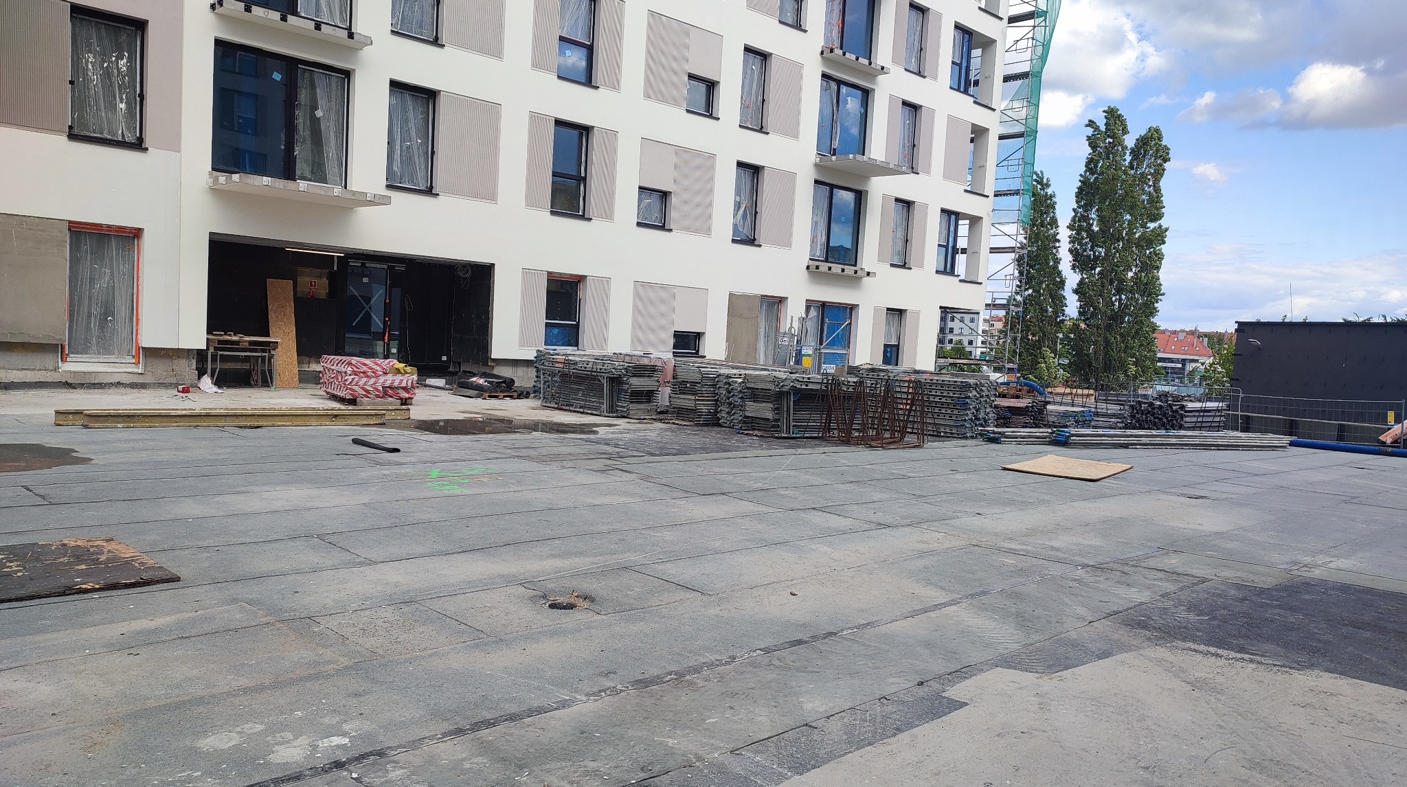 Wielopiętrowy budynek w trakcie prac elewacyjnych. Widoczne rusztowania, materiały budowlane i zabezpieczone okna folią. Jasna elewacja z elementami dekoracyjnymi.