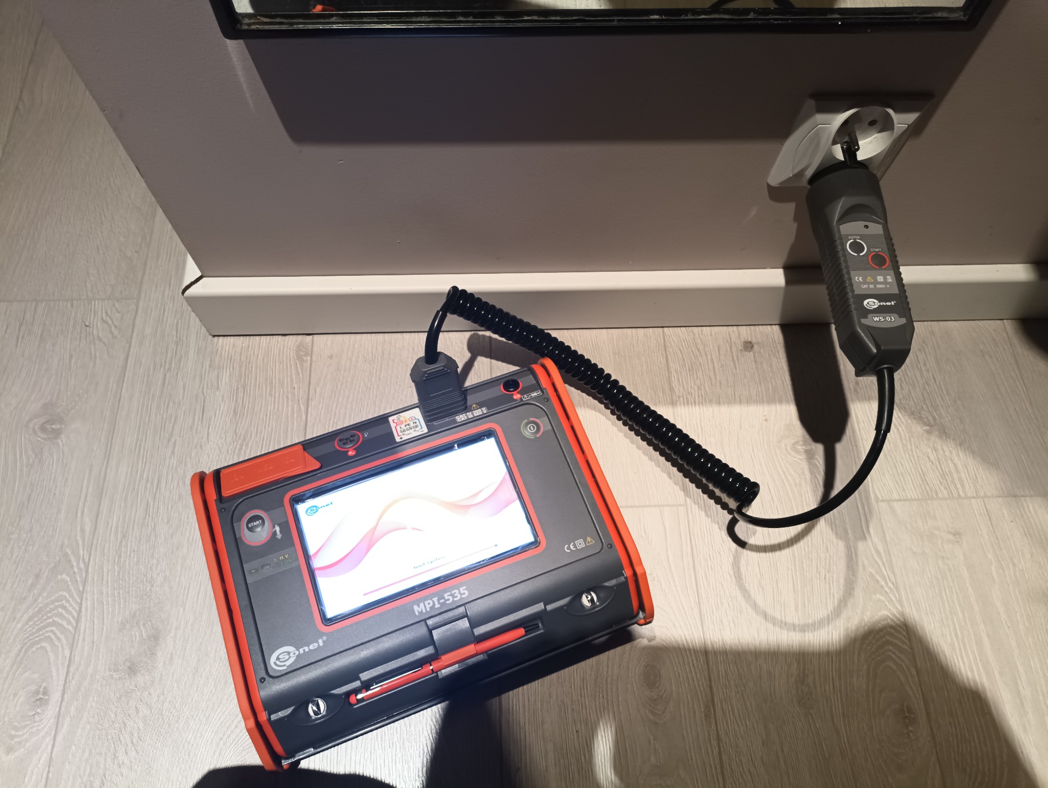 Miernik MPI-535 Sonel podłączony do gniazdka w Libiążu. Urządzenie do pomiarów elektrycznych leży na podłodze, gotowe do użycia. Widoczny przewód spiralny i wtyczka.