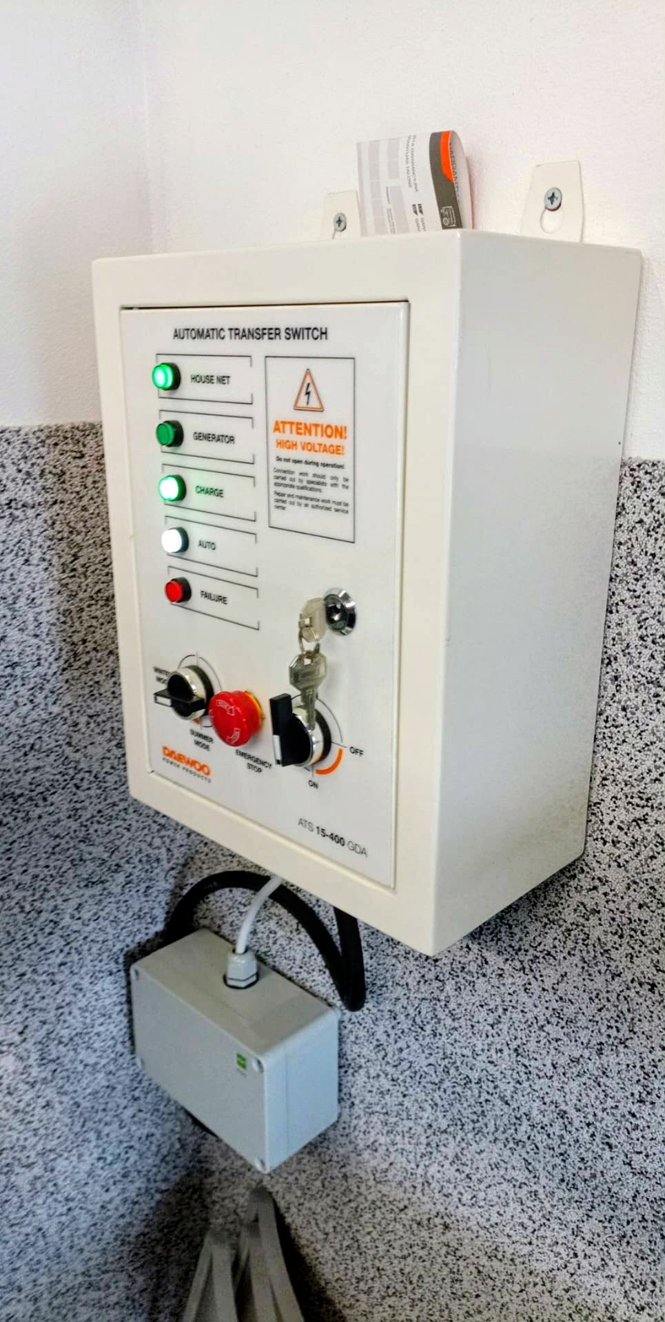 Biała skrzynka automatycznego przełącznika zasilania (ATS) Daewoo ATS 15-400 GDA, zamontowana na ścianie, z widocznymi diodami, przełącznikami i kluczykiem.