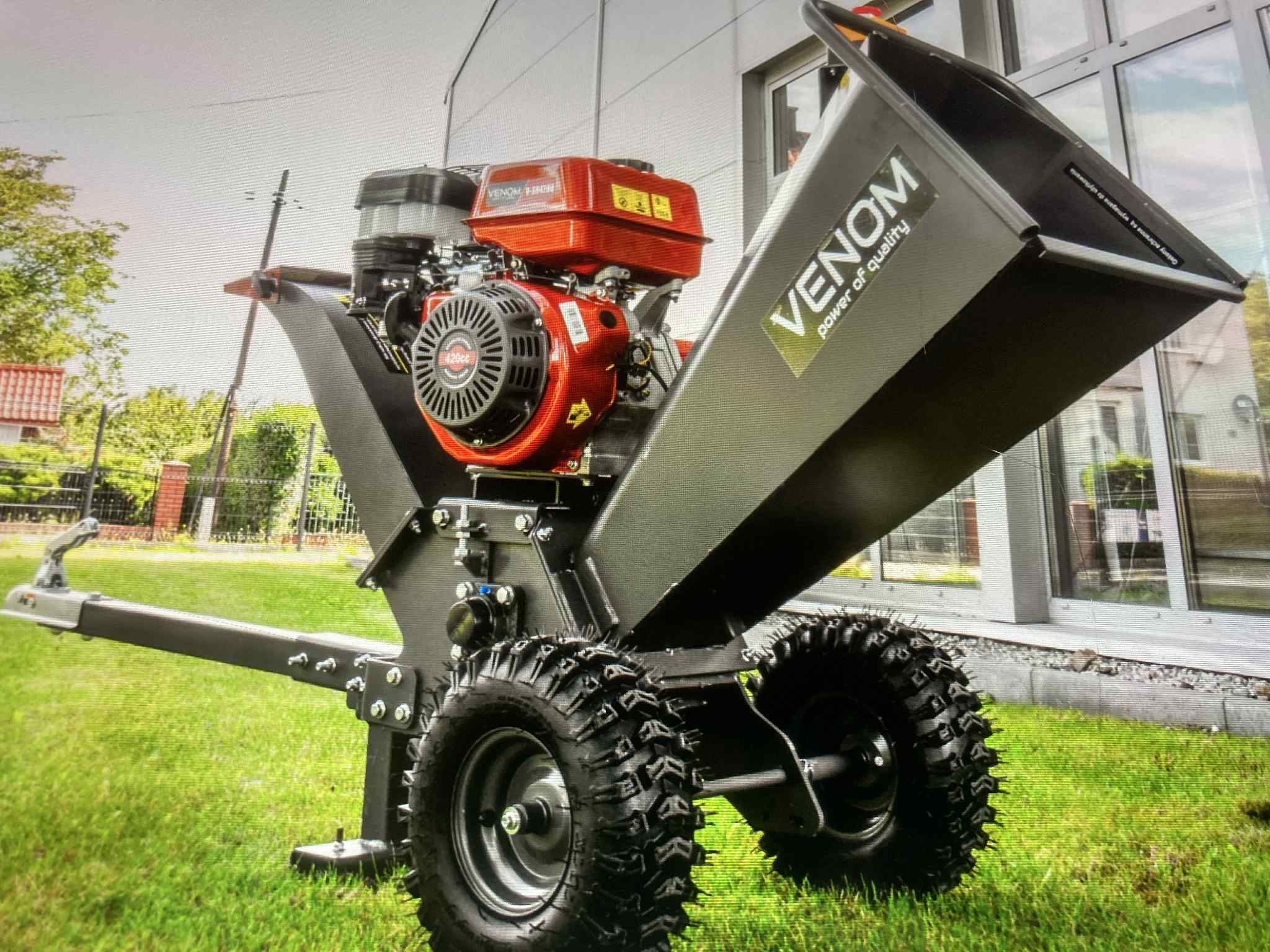 Mobilny rozdrabniacz do gałęzi Venom na trawie, z silnikiem spalinowym i dużymi oponami. Widoczny budynek z oknami w tle. Sprzęt ogrodniczy do wycinki drzew.