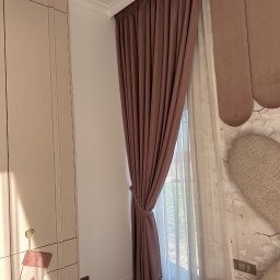 Eurofirany - Elegancka, marszczona zasłona w odcieniach brązu i beżu, upięta sznurem, z delikatną firaną w tle, tworząca przytulną atmosferę wnętrza.
