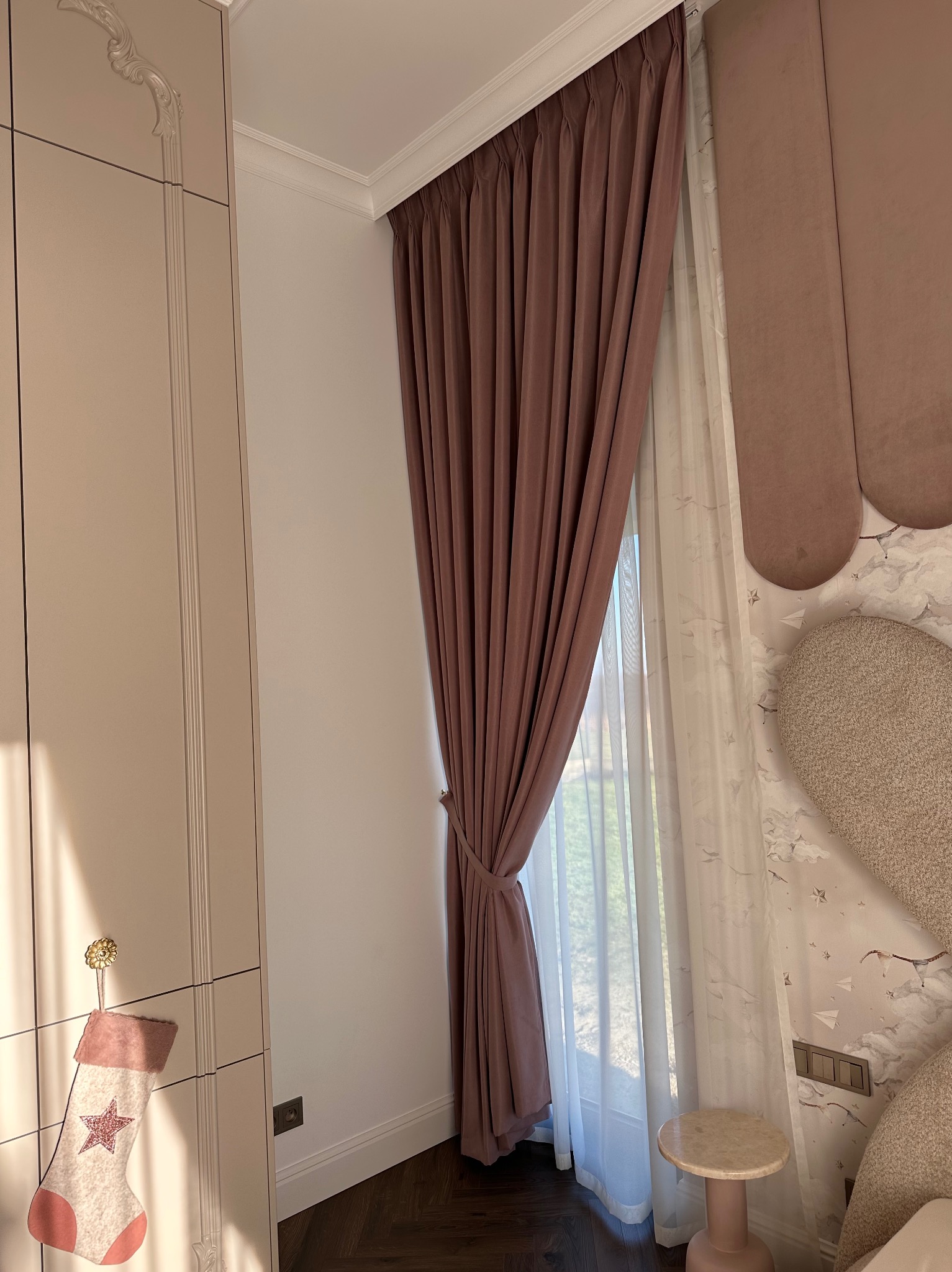 Elegancka, marszczona zasłona w odcieniach brązu i beżu, upięta sznurem, z delikatną firaną w tle, tworząca przytulną atmosferę wnętrza.