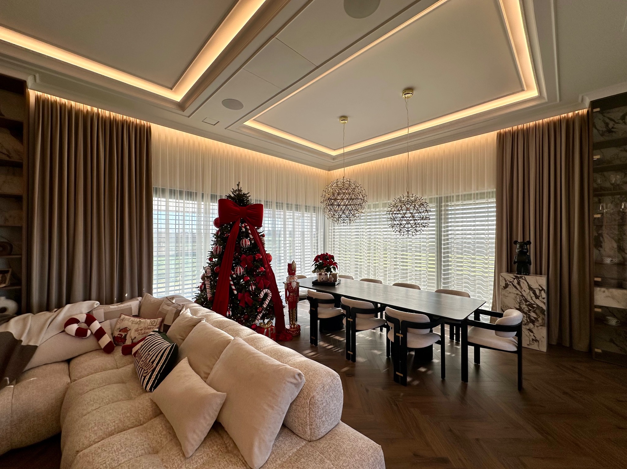 Elegancki salon z beżowymi zasłonami i roletami wewnętrznymi, świąteczny wystrój z choinką i dekoracjami. Nowoczesne oświetlenie sufitowe.