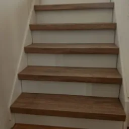 Wykończone schody wewnętrzne z drewnopodobnymi stopniami i białymi podstopnicami, widok z dołu, neutralne oświetlenie.