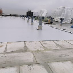 BKM Bud Katarzyna Wolińska - Montaż płyt Aquapanel na dachu budynku. Widoczne płyty cementowe, metalowe wsporniki i biała membrana. W tle rusztowania i zabudowy zabezpieczone folią.