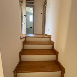 BKM Bud Katarzyna Wolińska - Drewniane schody z białymi podstopnicami prowadzą do jasnej łazienki z oknem. Widoczny klimatyzator i minimalistyczne oświetlenie sufitowe.