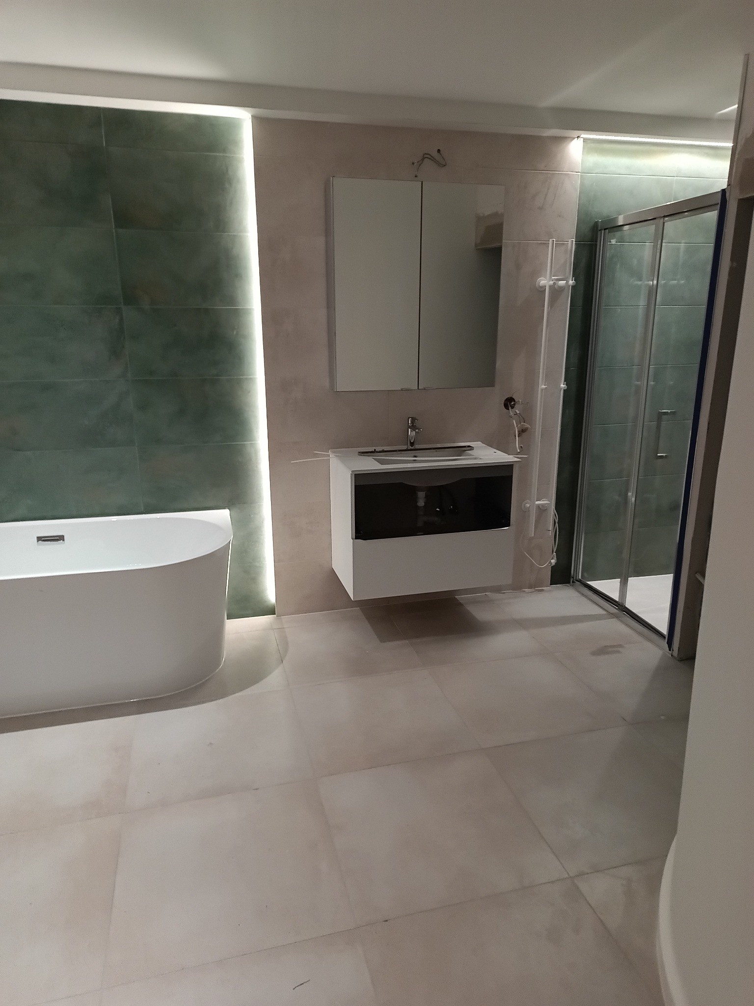 Nowoczesna łazienka po remoncie: wolnostojąca wanna, szafka z lustrem, kabina prysznicowa. Stonowana kolorystyka, podświetlenie LED. Widok na całe pomieszczenie.