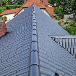 Star sp. z o.o. - Szary, ceramiczny dach z widoczną dachówką karpiówką, z kominem w tle i fragmentem okna dachowego w prawym dolnym rogu. Widok z góry na tle zabudowy.