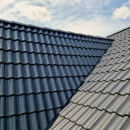 Czarny dach z dachówki ceramicznej, widziany z góry, na tle błękitnego nieba w Kiełczowie. Widoczny fragment kalenicy.