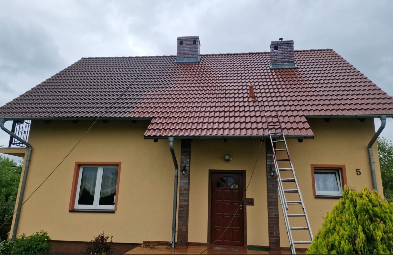 Ukończony etap mycia dachu z czerwonej dachówki. Część dachu umyta, część brudna. Metalowa drabina oparta o elewację domu. Widoczne dwa kominy.