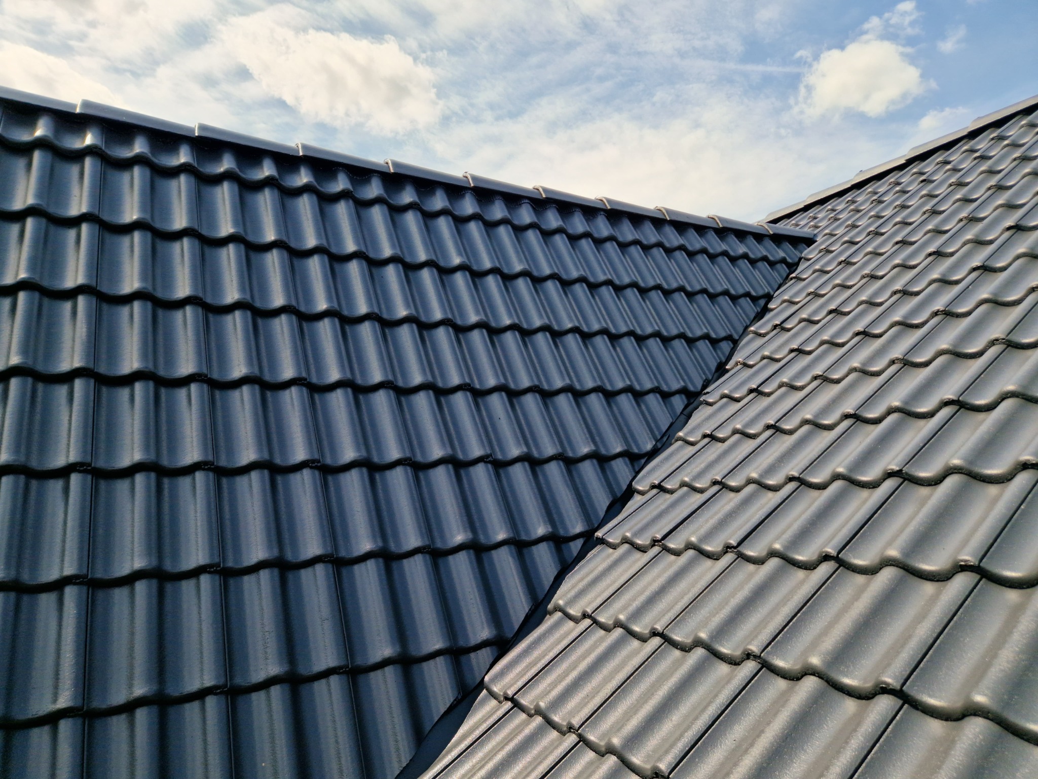 Czarny dach z dachówki ceramicznej, widziany z góry, na tle błękitnego nieba w Kiełczowie. Widoczny fragment kalenicy.