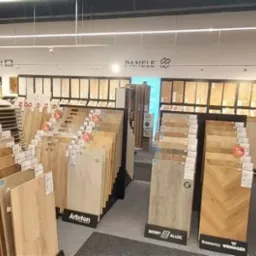 Ekspozycja paneli podłogowych w sklepie: różnorodne wzory i kolory, od jasnych po ciemne drewno, marki Arbiton, Berry Alloc, Kronospan Wenninger. Promocja -15%.