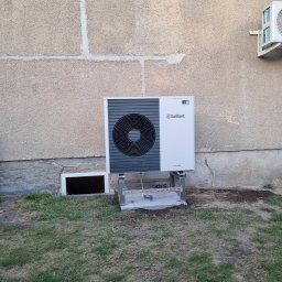 Technika Grzewcza Marcin Kowalczyk - Zamontowana pompa ciepła Vaillant aroTHERM na zewnątrz budynku z widocznym innym urządzeniem klimatyzacyjnym na ścianie. Widok na trawnik.