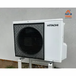 Biała zewnętrzna jednostka klimatyzacji Hitachi, zamontowana na metalowym stelażu przy jasnej ścianie budynku. Widoczne logo firmy MAT HVAC w prawym górnym rogu.