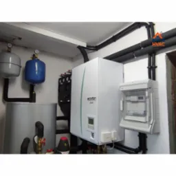 Wnętrze kotłowni z zainstalowaną pompą ciepła Ecodan, zbiornikiem buforowym i rozdzielnicą elektryczną. Rury instalacyjne prowadzone wzdłuż ścian.