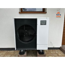 Mat HVAC - Biała pompa ciepła Mitsubishi Zubadan R32, zamontowana na zewnątrz budynku. Widoczny wentylator i logo producenta. Tło stanowi biała ściana i okno.