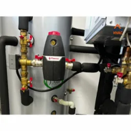 Szczegółowe ujęcie instalacji hydraulicznej z zaworami, rurami i czarnym separatorem powietrza Flamco, zamontowanej przy srebrnym zbiorniku. Widoczne elementy instalacji grzewczej.