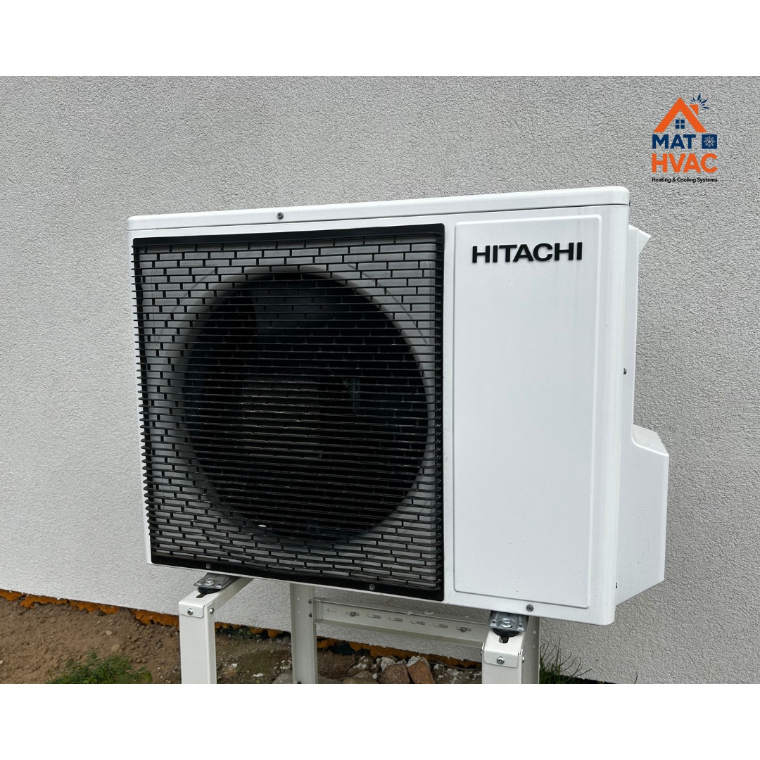 Biała zewnętrzna jednostka klimatyzacji Hitachi, zamontowana na metalowym stelażu przy jasnej ścianie budynku. Widoczne logo firmy MAT HVAC w prawym górnym rogu.