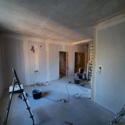 Przedsiębiorstwo Budowlane Paweł Sydlewski - Wnętrze w trakcie prac wykończeniowych: ściany z płyt karton-gips, częściowo zagruntowane, widoczne kable, drabina i narzędzia malarskie. Przygotowanie do dalszych prac.