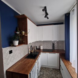 Przedsiębiorstwo Budowlane Paweł Sydlewski - Nowoczesna kuchnia w odcieniach bieli, drewna i granatu. Uwagę przykuwają drewniane blaty, białe szafki z frezowanymi frontami i wzorzysta podłoga.