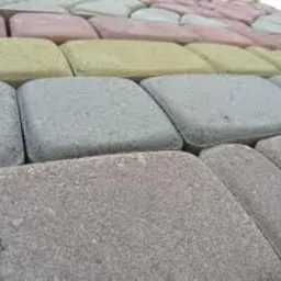 Powierzchnia wyłożona kostką brukową w odcieniach szarości, różu i żółci, ułożona w regularny wzór. Widoczny fragment nawierzchni z bliska, ukazujący fakturę poszczególnych elementów.