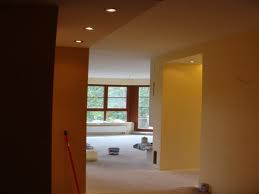 Wnętrze w trakcie remontu: świeżo pomalowane ściany w odcieniach beżu i żółci, widoczne puszki z farbą, surowe wykończenie podłogi, okno z widokiem na zieleń.