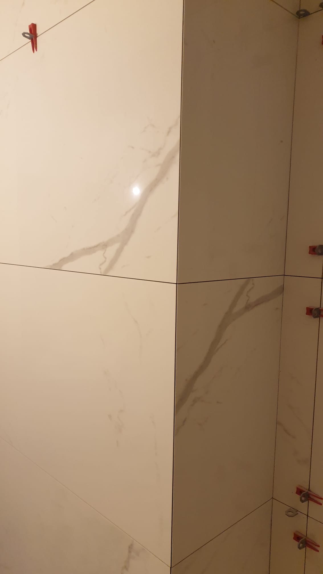 Ściana wyłożona jasnymi płytkami imitującymi marmur, z widocznymi klipsami poziomującymi, ukazująca precyzję układania i dbałość o detale.