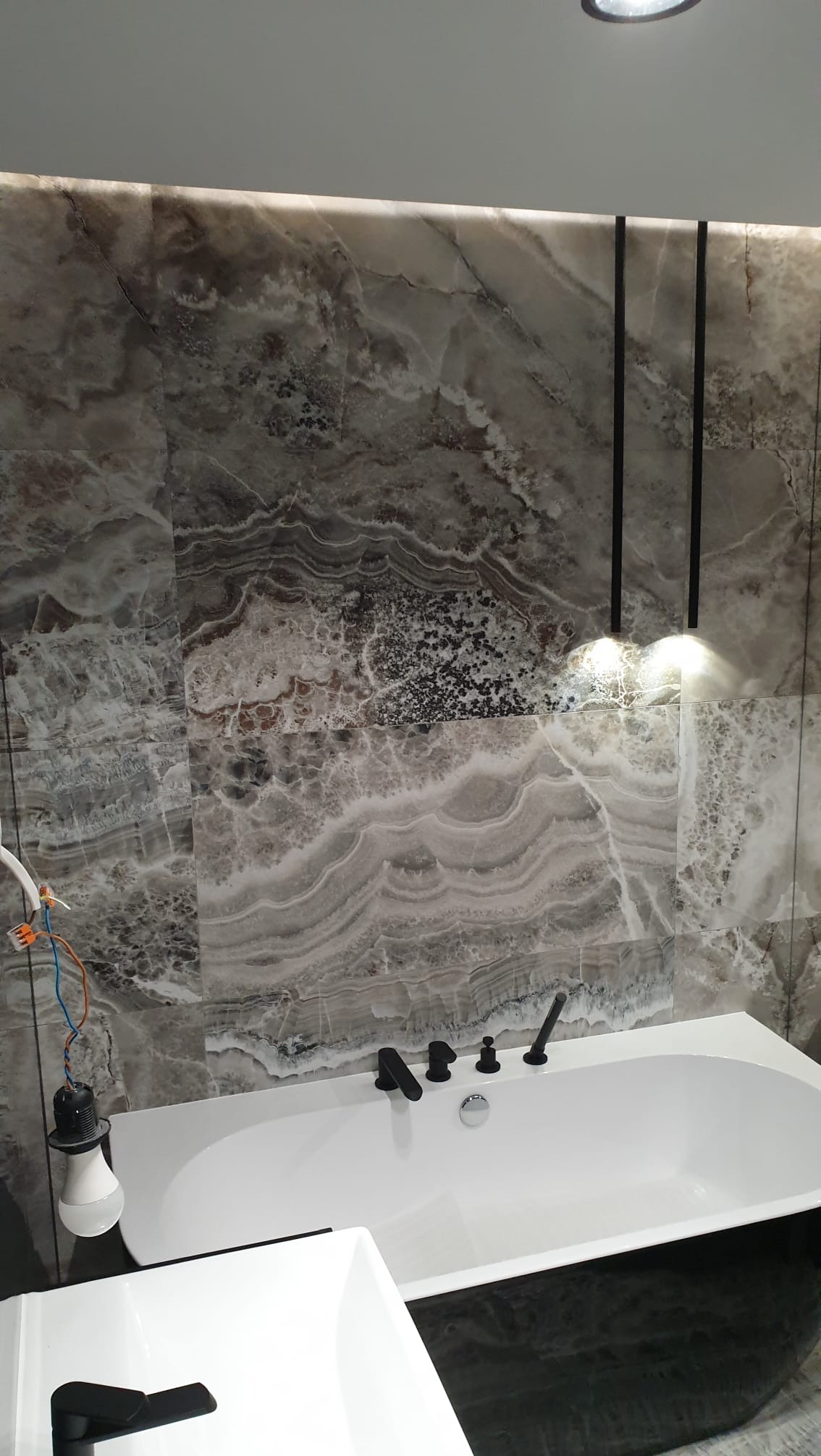 Wykończona łazienka w Starych Bielicach: marmurowe płytki na ścianach, biała wanna z czarną armaturą i wiszące lampy. Nowoczesny design.