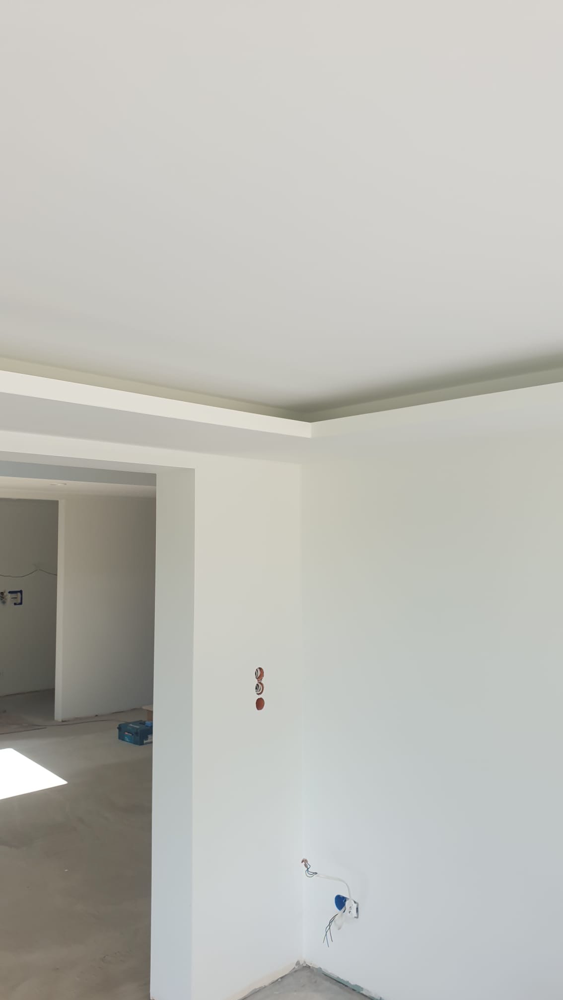 Wnętrze po szpachlowaniu i malowaniu na biało, z widocznymi puszkami elektrycznymi i otworami na gniazdka. Surowa podłoga, brak listew przypodłogowych.