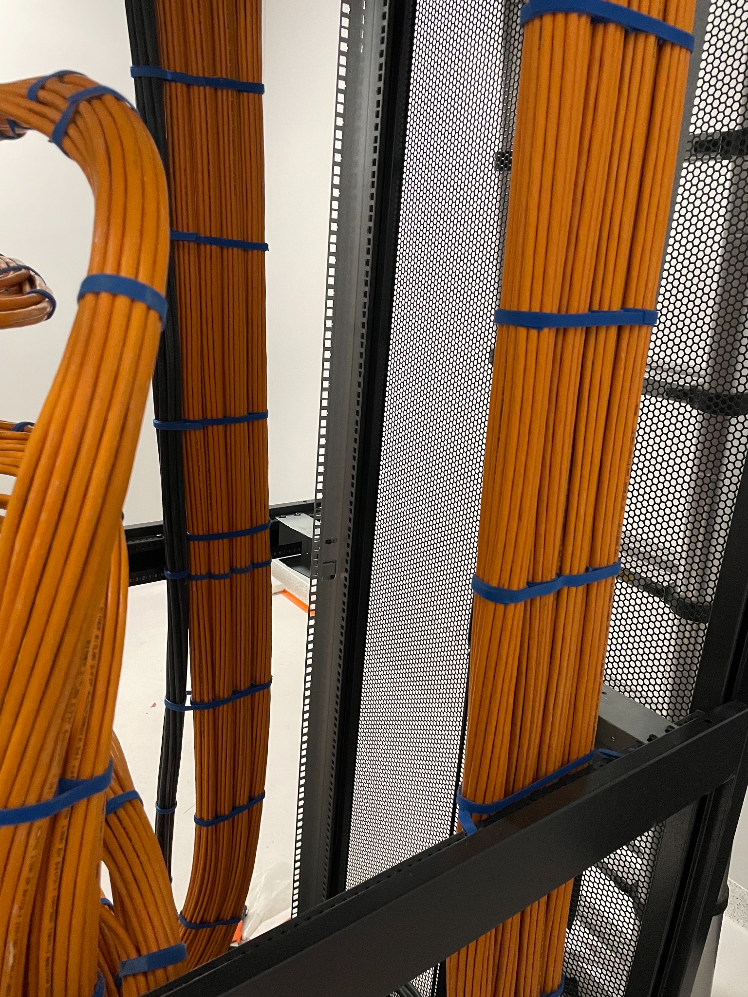 Pomarańczowe kable uporządkowane w szafie serwerowej, zabezpieczone niebieskimi opaskami. Widoczne metalowe elementy konstrukcji szafy.
