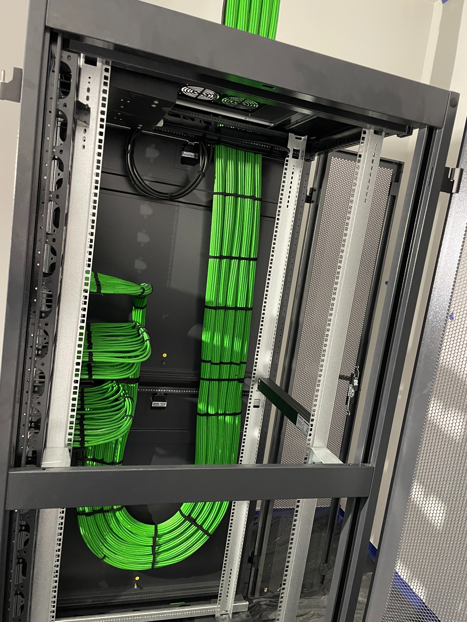 Szafa serwerowa z uporządkowanymi, zielonymi kablami. Profesjonalny montaż przewodów w serwerowni. Estetyczne i funkcjonalne rozwiązanie.