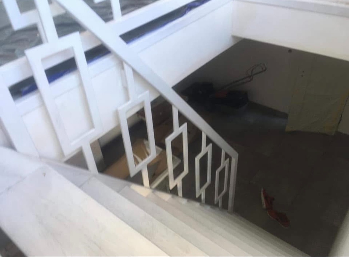 Białe schody z nowoczesną balustradą z geometrycznym wzorem, widok z góry. Na podeście leżą narzędzia i pojedynczy but, co sugeruje trwające prace wykończeniowe.