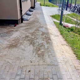 MIROSŁAW OCZKOWSKI KAMIR-BUD - Świeżo ułożona kostka brukowa przy budynku, z widocznymi śladami piasku i ziemi, oczekująca na ostateczne wyczyszczenie i zagęszczenie.