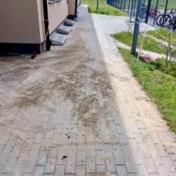 Świeżo ułożona kostka brukowa przy budynku, z widocznymi śladami piasku i ziemi, oczekująca na ostateczne wyczyszczenie i zagęszczenie.