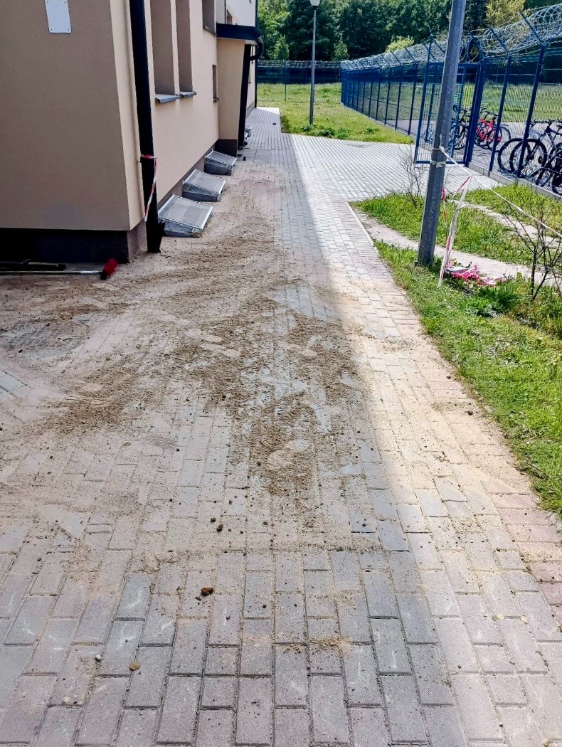 Świeżo ułożona kostka brukowa przy budynku, z widocznymi śladami piasku i ziemi, oczekująca na ostateczne wyczyszczenie i zagęszczenie.