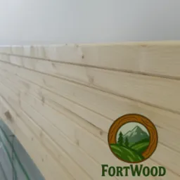 Jasne, świerkowe deski boazeryjne ułożone poziomo, z delikatnym rysunkiem słojów. Widoczne logo producenta FortWood. Ujęcie z bliska, podkreślające fakturę drewna.