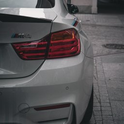 Albert Szymański - Białe BMW M4 z widocznymi tylnymi światłami, spojlerem i emblematem M. Ujęcie z bliska, podkreślające detale i sportowy charakter auta na tle miejskiej kostki.