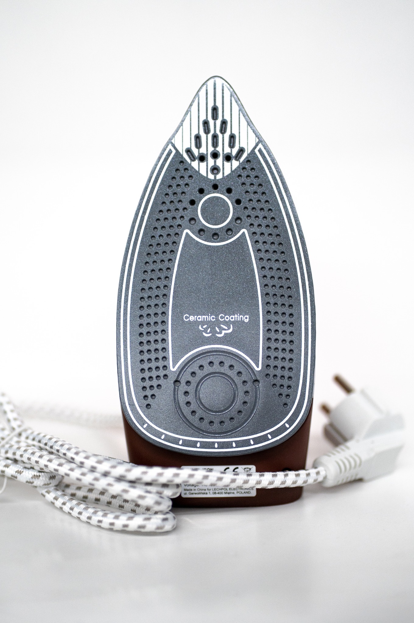 Żelazko z ceramiczną powłoką, widoczne otwory parowe i kabel zasilający, ustawione na białym tle. Ujęcie z bliska, skupione na stopie żelazka.