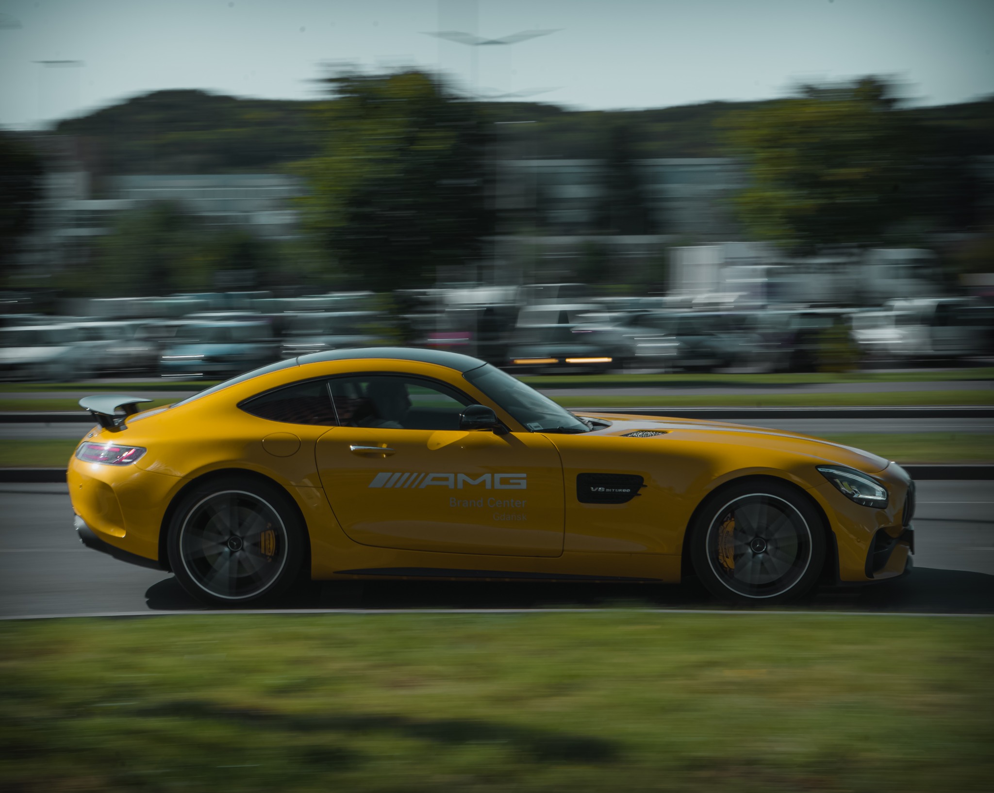 Dynamiczne ujęcie żółtego samochodu sportowego AMG w ruchu, z rozmytym tłem miejskim. Widoczne detale karoserii i logo. Zdjęcie w ruchu, podkreślające prędkość i nowoczesny design.