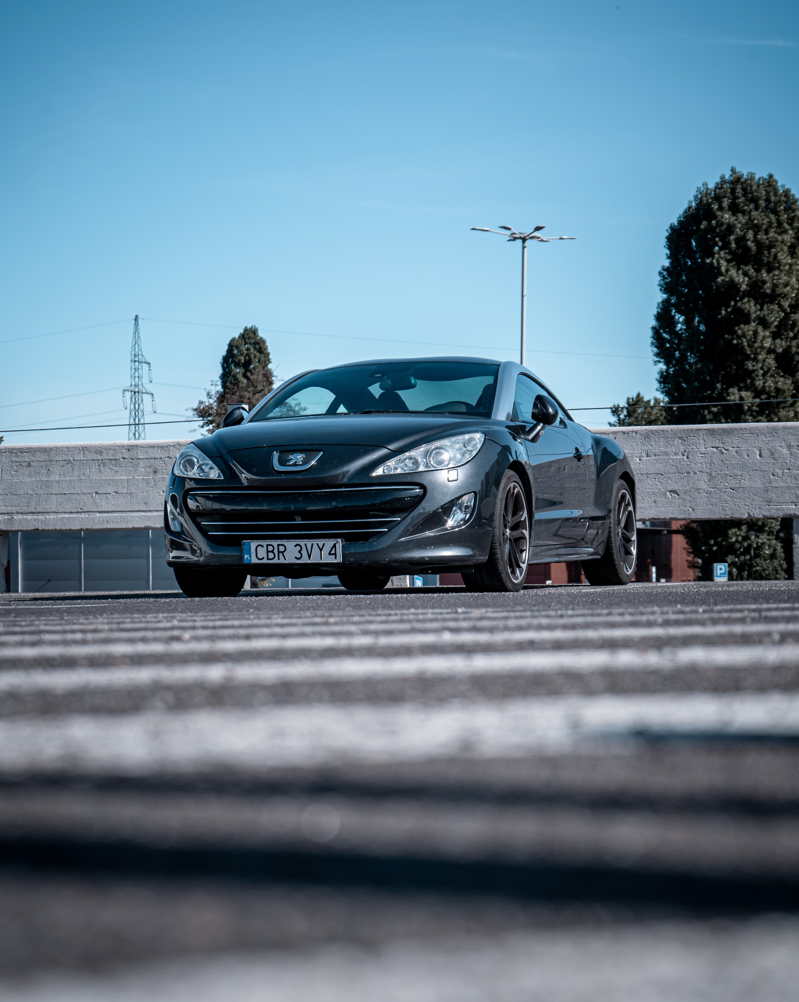 Szary Peugeot RCZ z gdańską tablicą rejestracyjną CBR 3VY4 na parkingu, uchwycony z niskiej perspektywy, podkreślającej sportowy charakter auta.