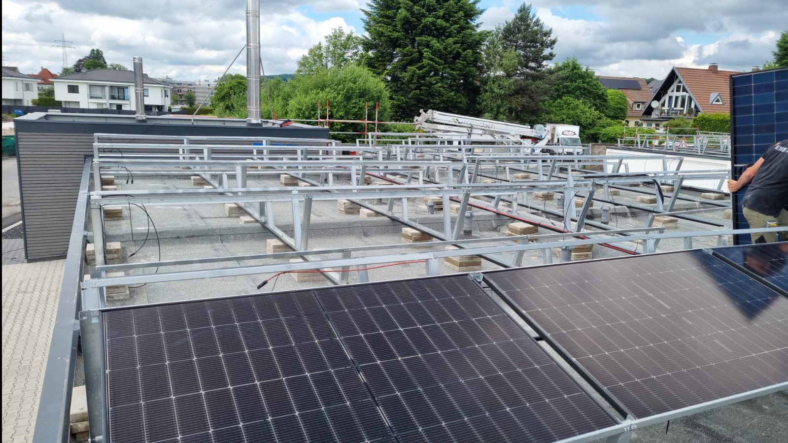 Montaż paneli słonecznych na dachu budynku w Witkowie. Widoczne panele, metalowa konstrukcja wsporcza i pracownik. W tle zabudowa miejska i zieleń.